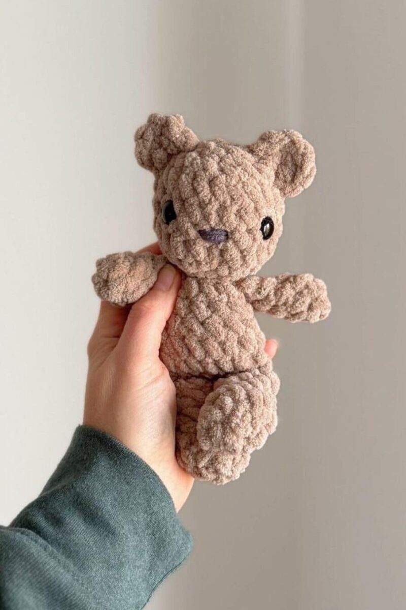 Hand holding a little brown crochet bear.