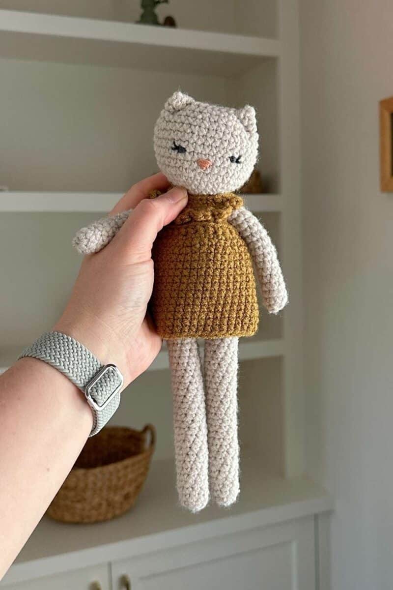 Hand holding a crochet cat wearing a dress.