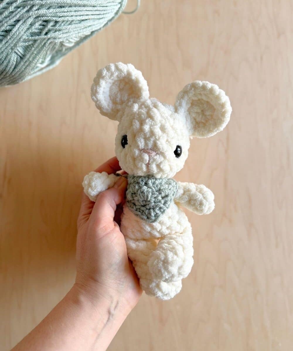 Hand holding a baby crochet mouse with a blue neckerchief on.