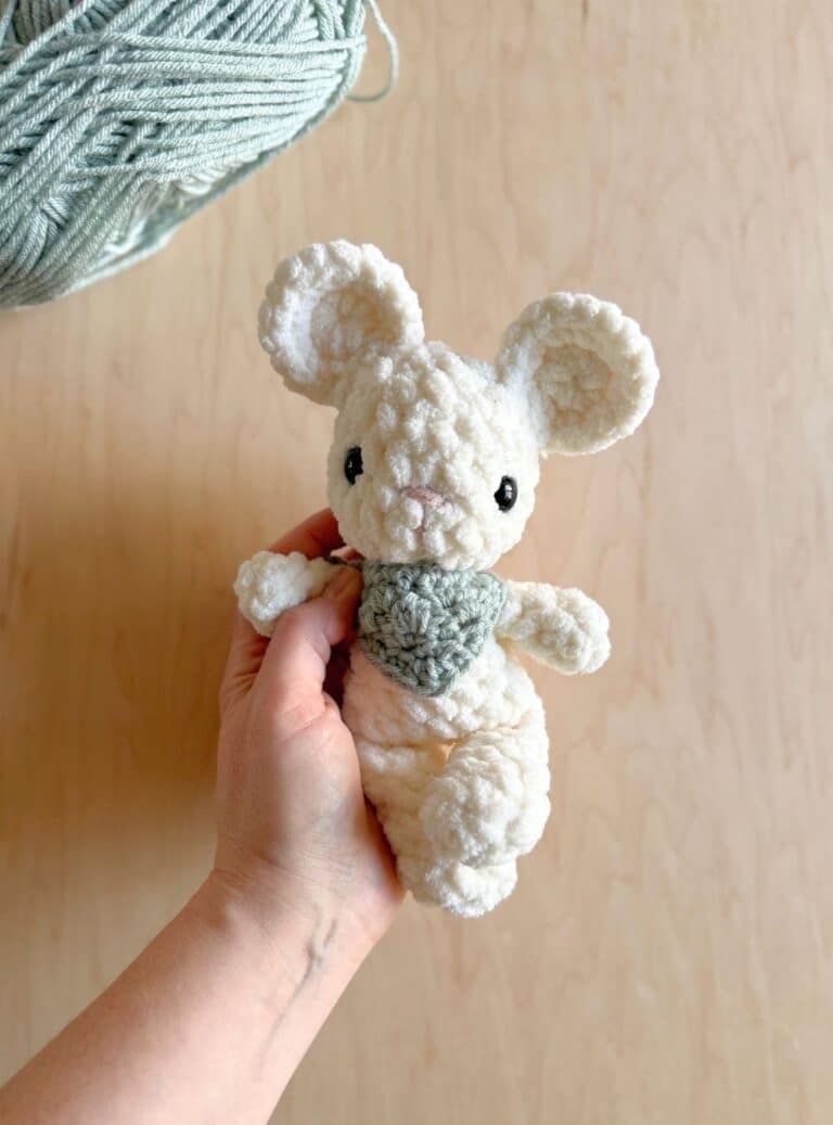 Hand holding a baby crochet mouse with a blue neckerchief on.
