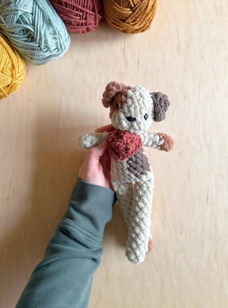 Hand holding a spotted crochet dog wearing a red neckerchief.