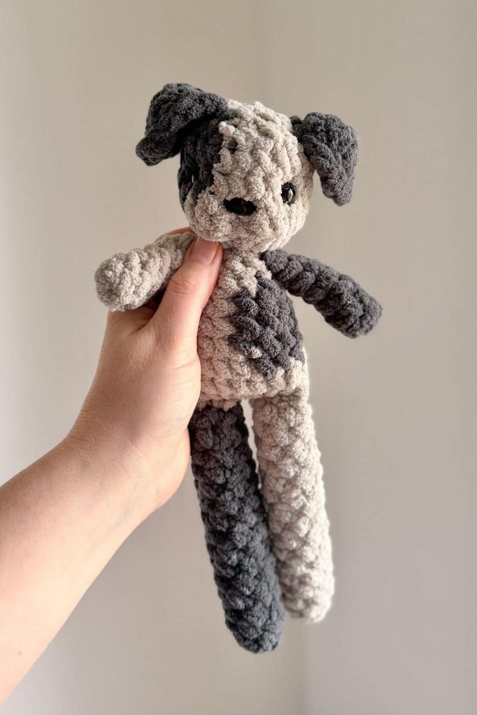 Hand holding a little spotted grey dog with long legs.