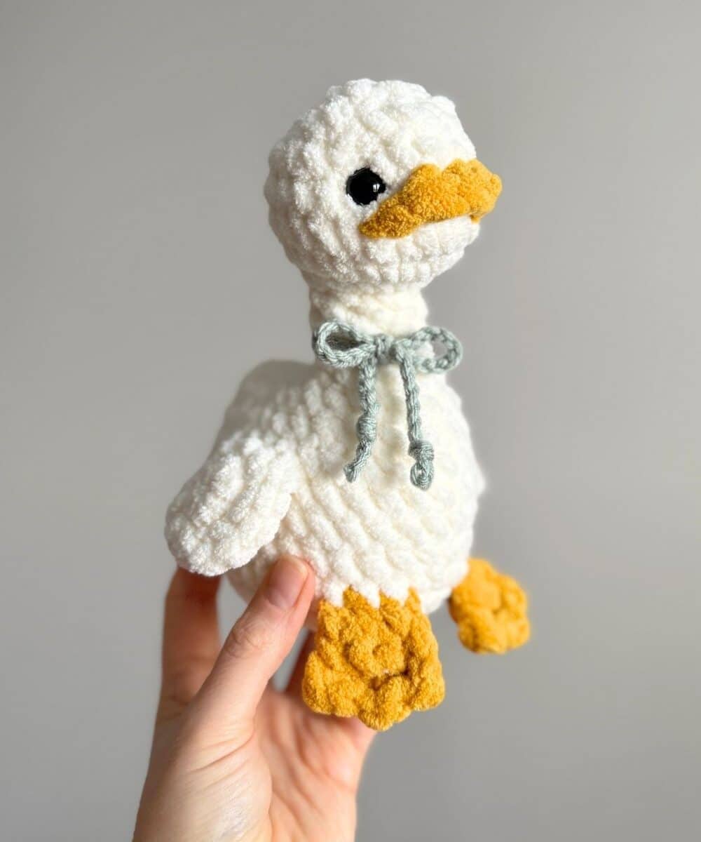 A white crochet goose with a blue bow on her neck.