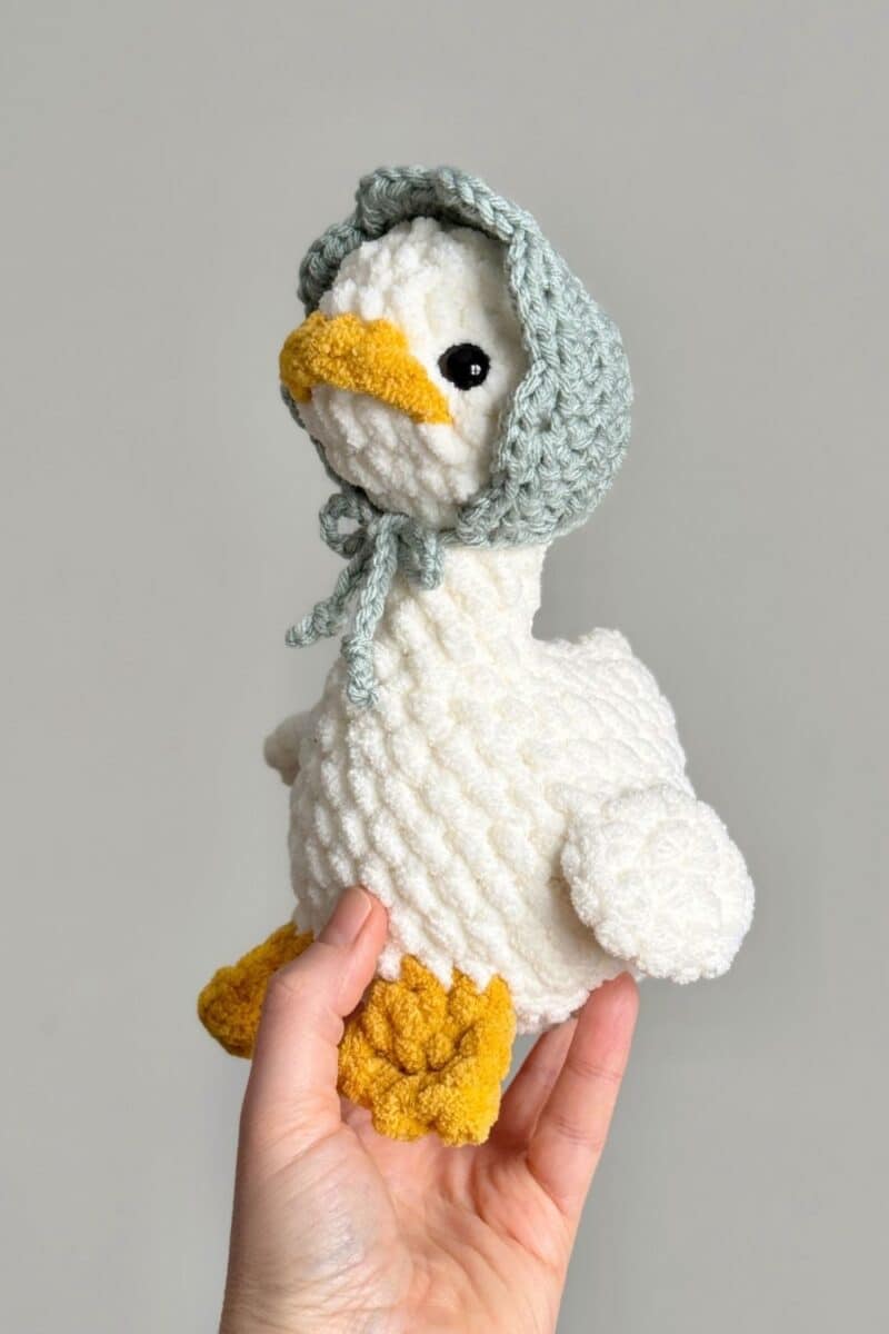 A crochet goose wearing a blue crochet bonnet.