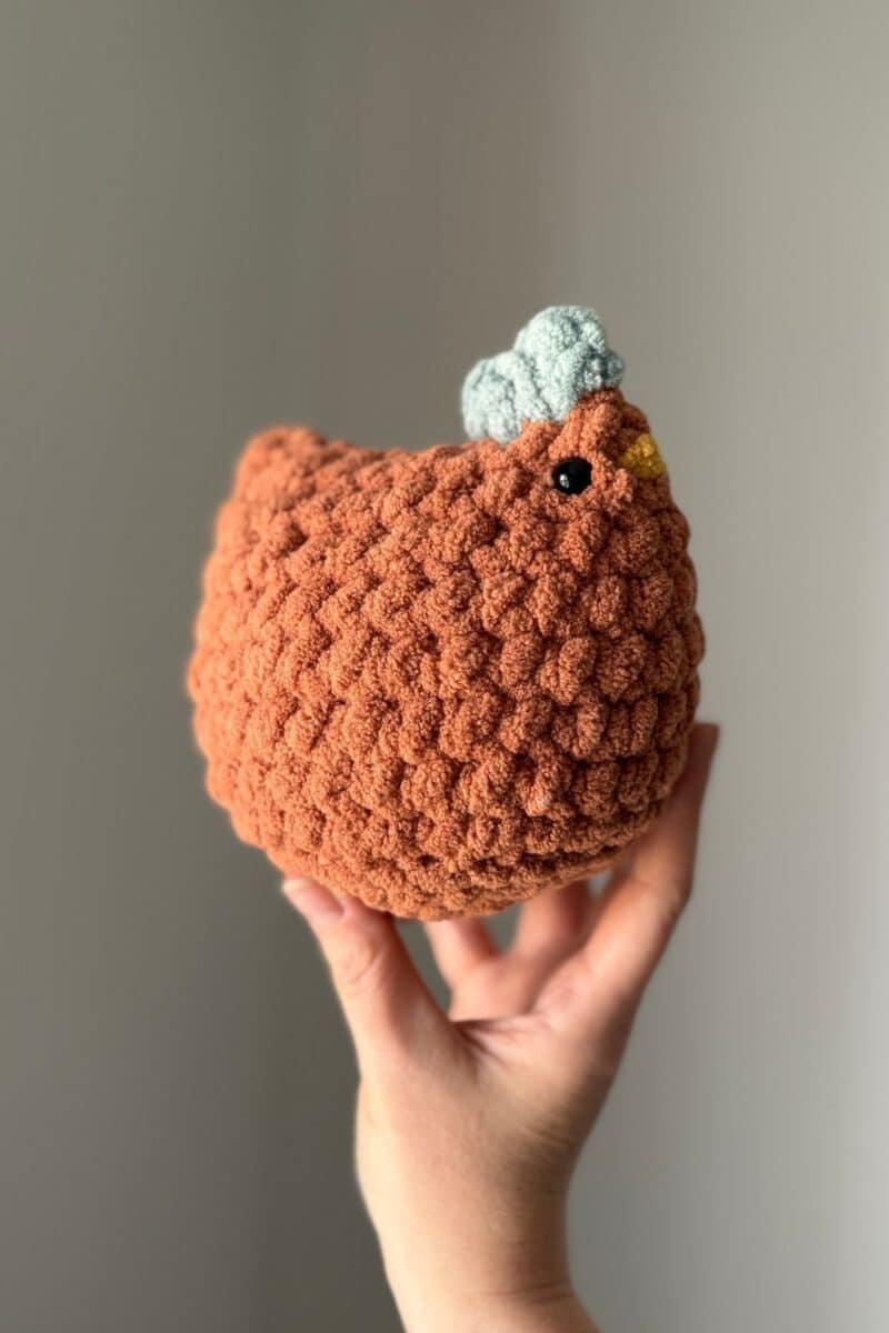 An orange colored crochet chicken with a blue comb.