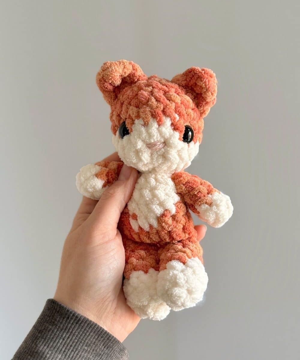 A baby crochet kitten made with orange and cream yarn.