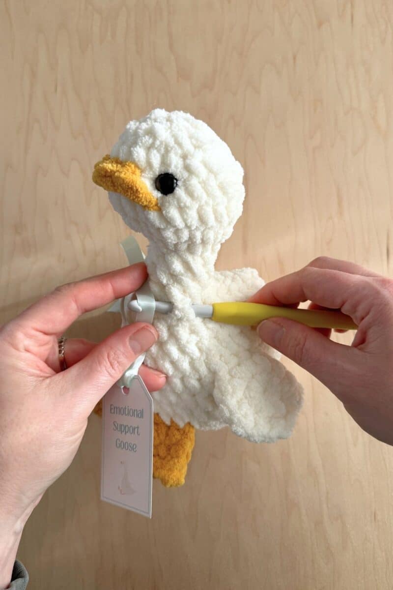 Hands inserting a crochet hook into a crochet goose to weave a ribbon in.
