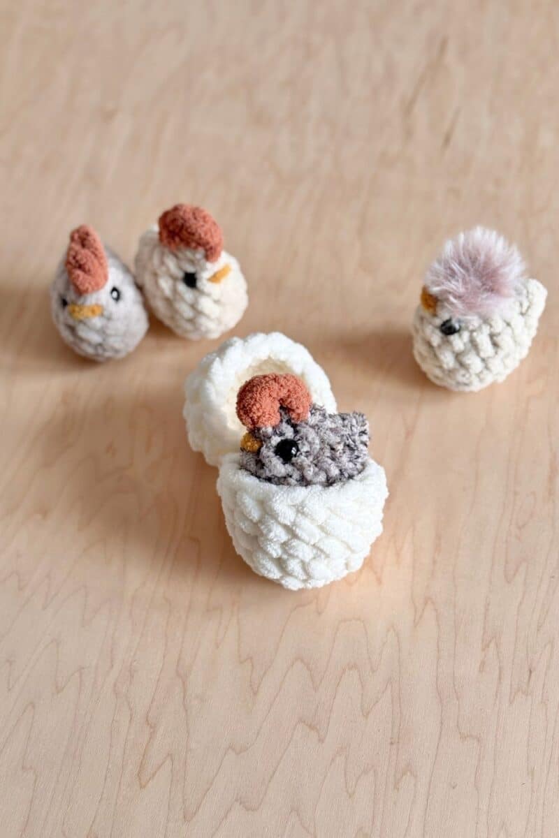 A tiny crochet chicken in a hatching egg with other little chickens in the background.