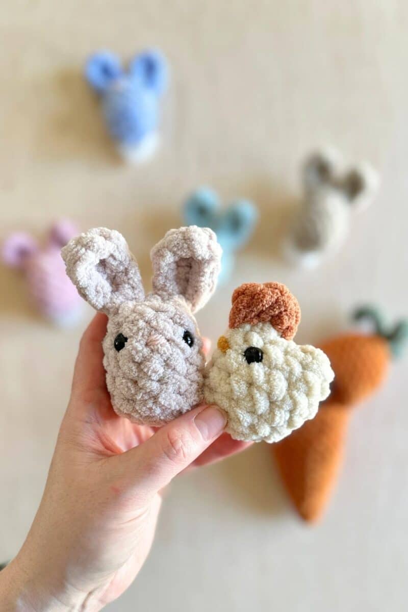 A crochet bunny and chicken with more bunnies and a carrot in the background.