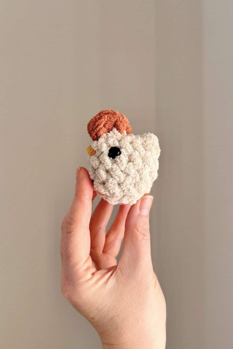 Hand holding a little crochet chicken with a blanket yarn comb.