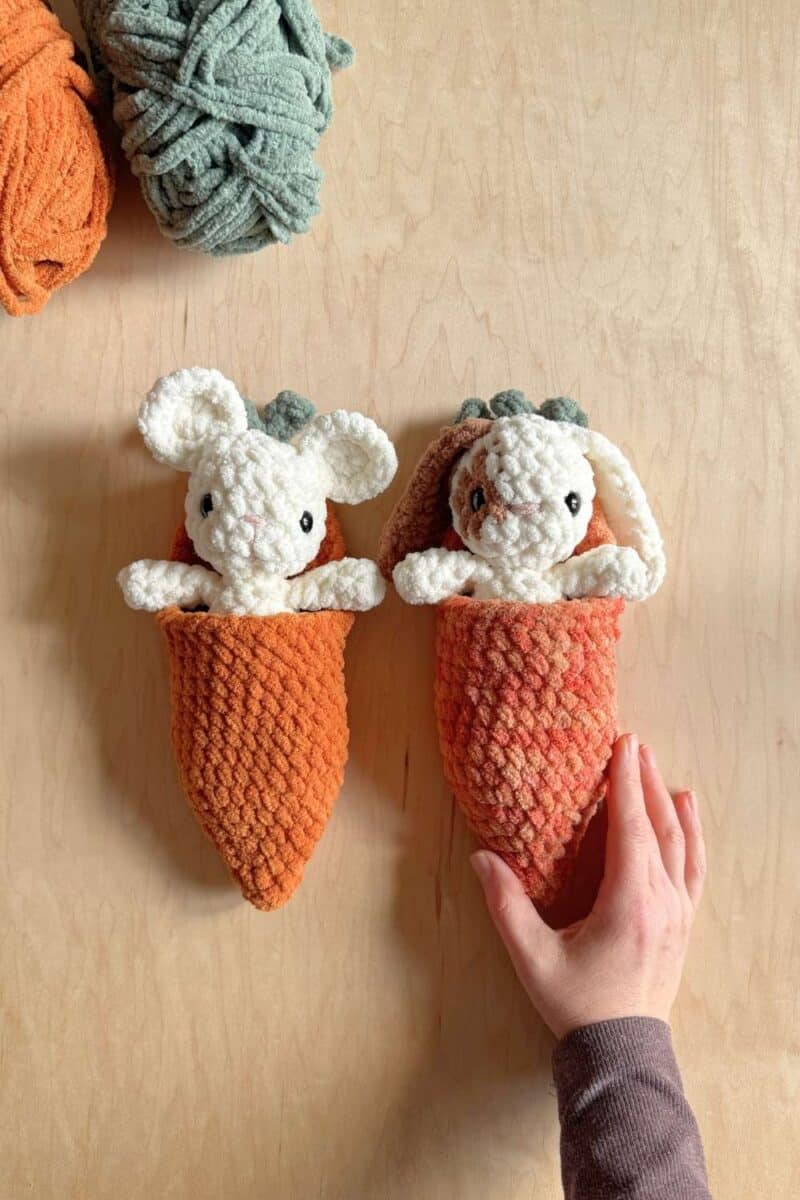 A white crochet mouse and a patchy crochet bunnies both inside carrot sleeping bags.