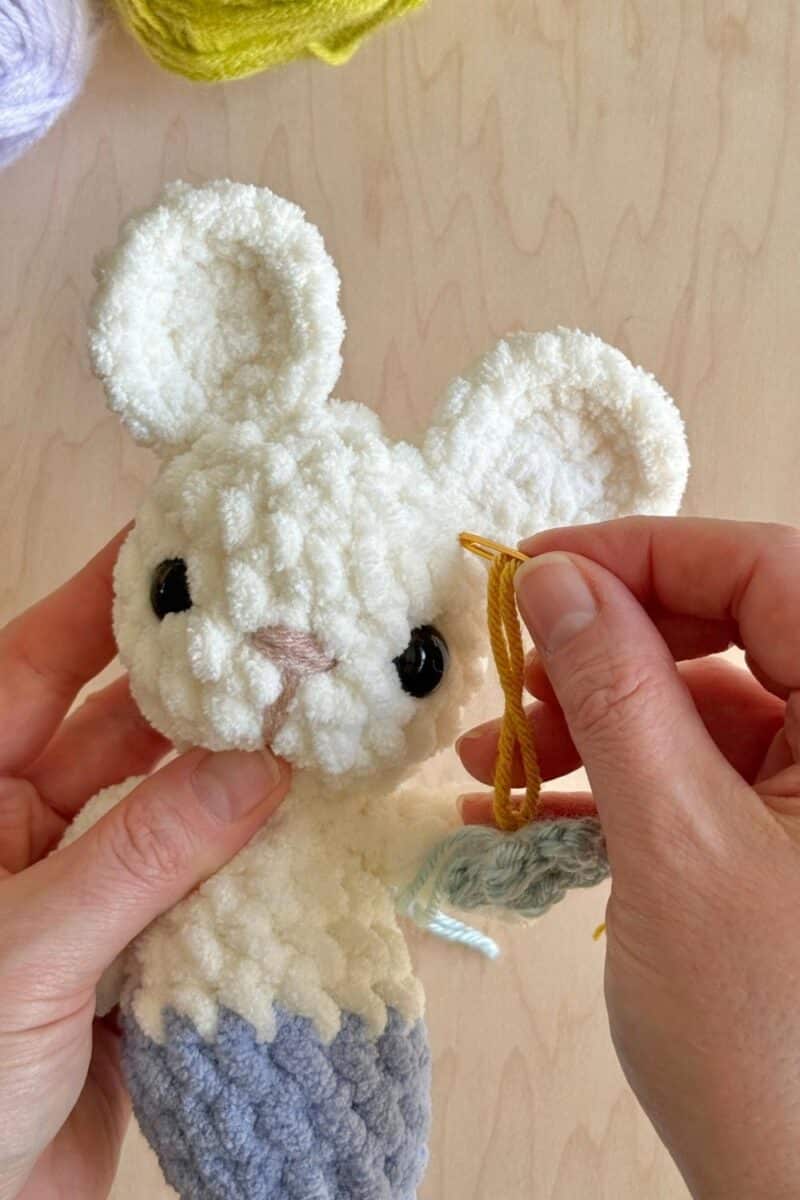 Using a yarn needle to weave end of flower into the head.