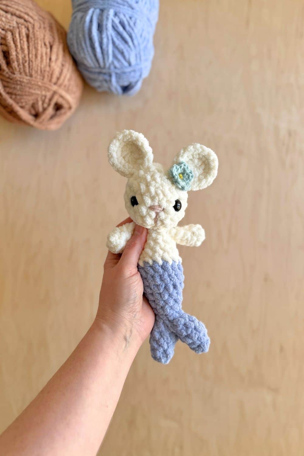 Hand holding a white crochet mer-mouse wearing a tiny crochet flower on her ear.