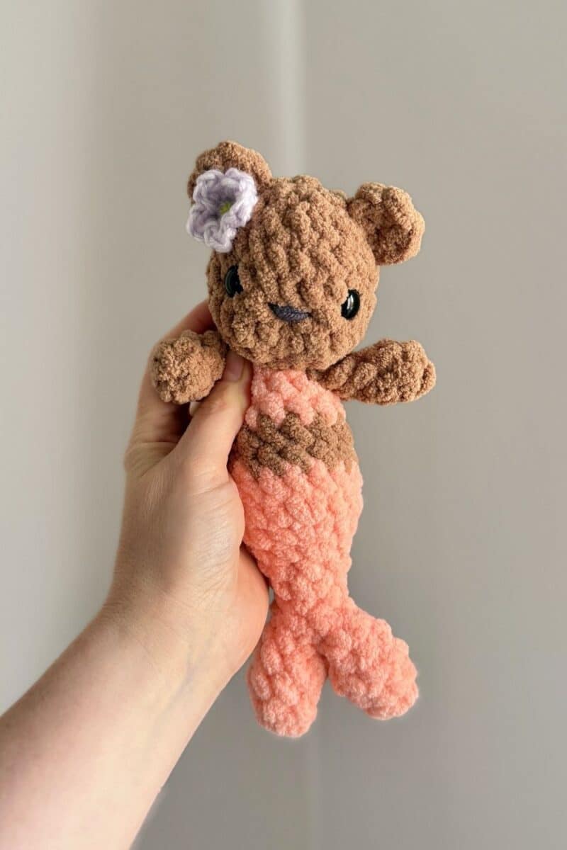 Hand holding a little crochet mer-bear with a pink tail and top.