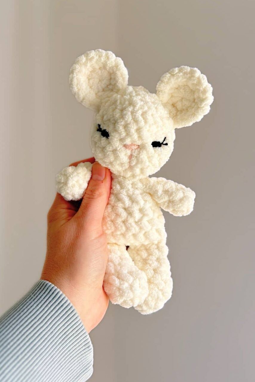 Hand holding a white crochet mouse with embroidered eyes.