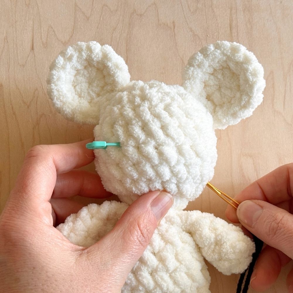 A stitch marker marking eyes on a white crochet mouse head.