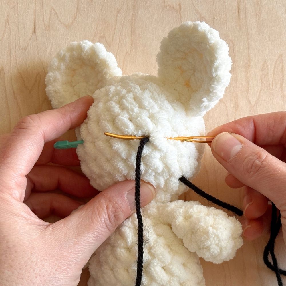 Showing first steps of embroidering the eye on a crochet mouse.