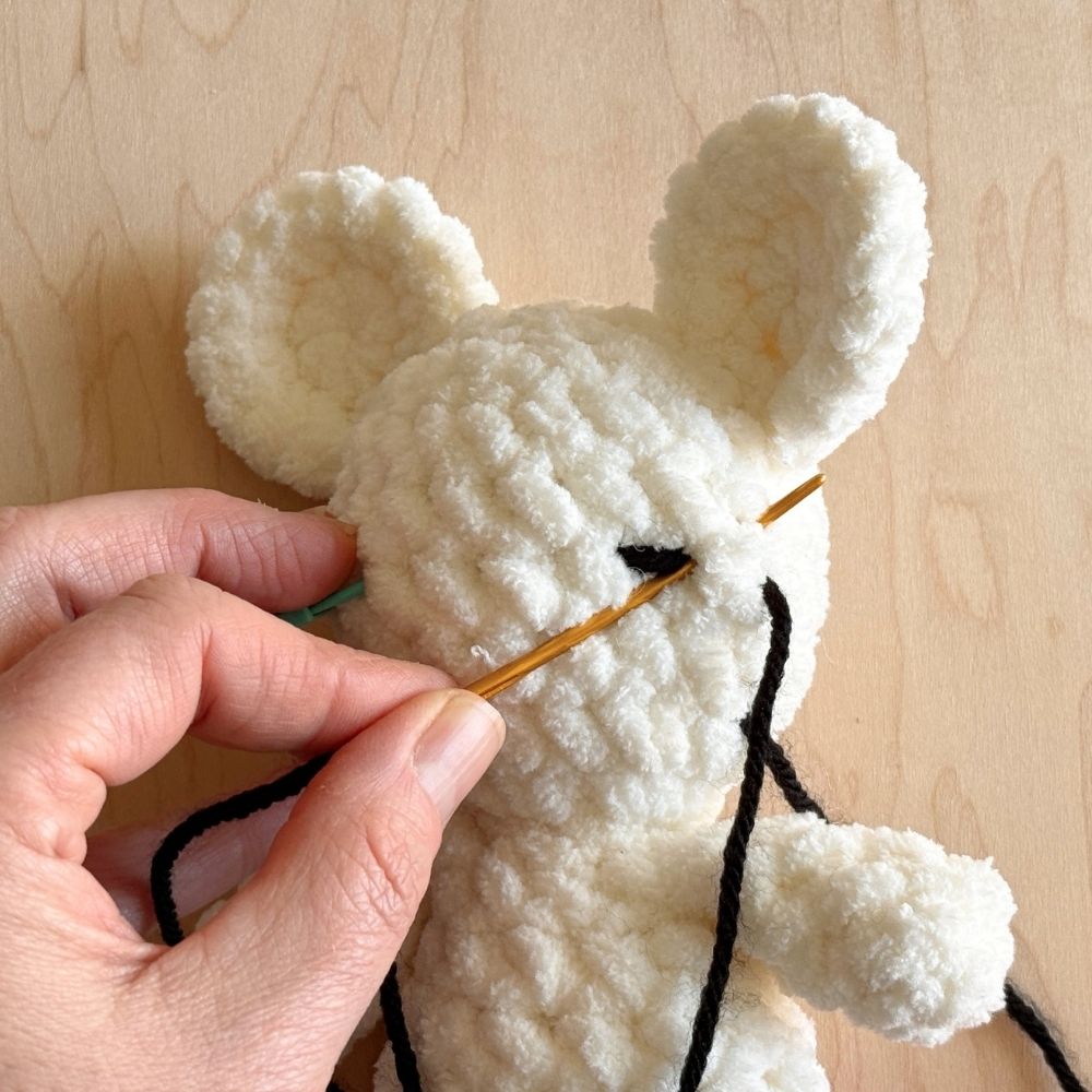 Showing first steps of embroidering the eye lash on the eye on a crochet mouse.