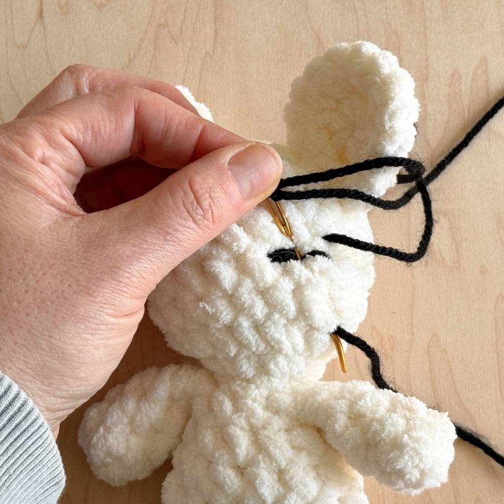 Making the second embroidered eyelash on a crochet mouse.