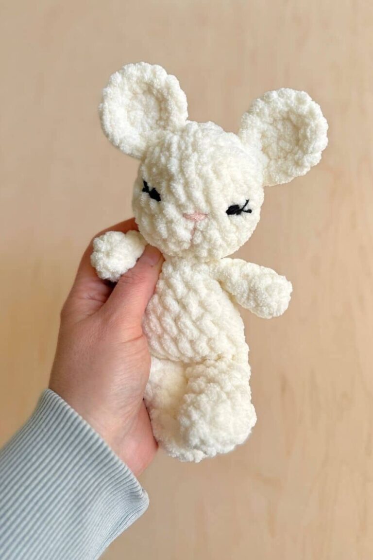 Hand holding a crochet mouse with embroidered eyes.