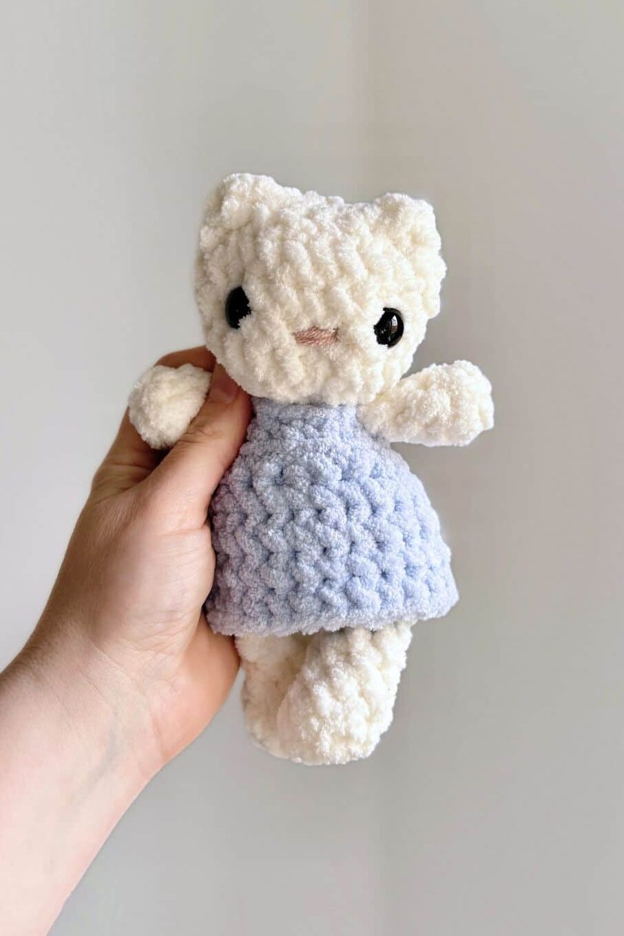 hand holding a white crochet baby kitty in a blue dress.