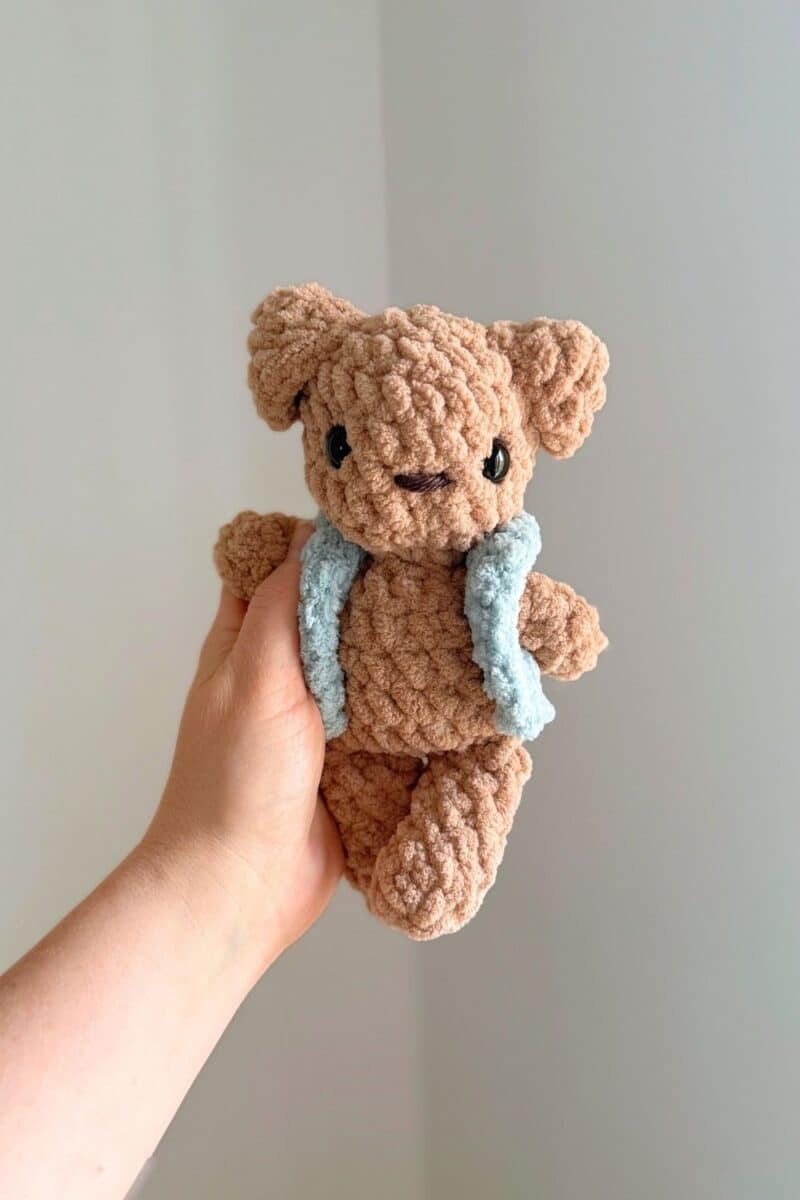 Hand holding a brown crochet dog wearing a little blue crochet vest.