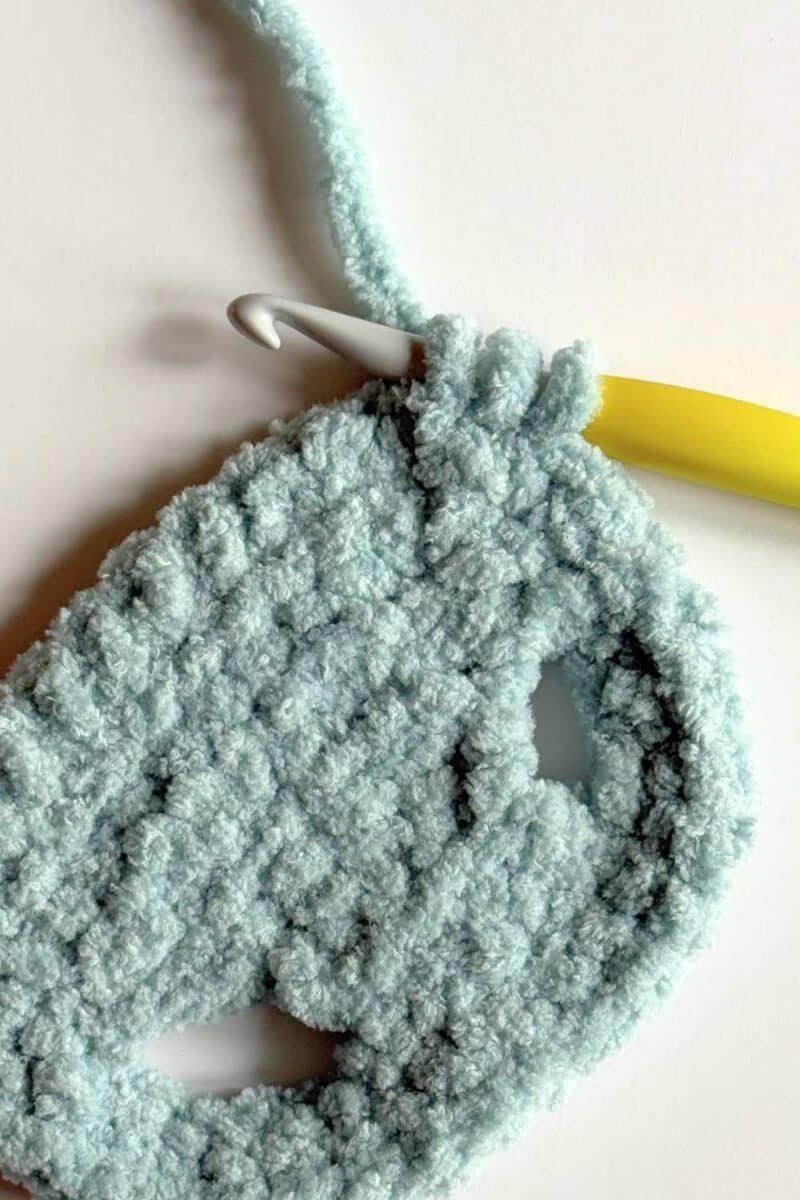 Three loops on a crochet hook to complete the corner of a blue crochet vest.
