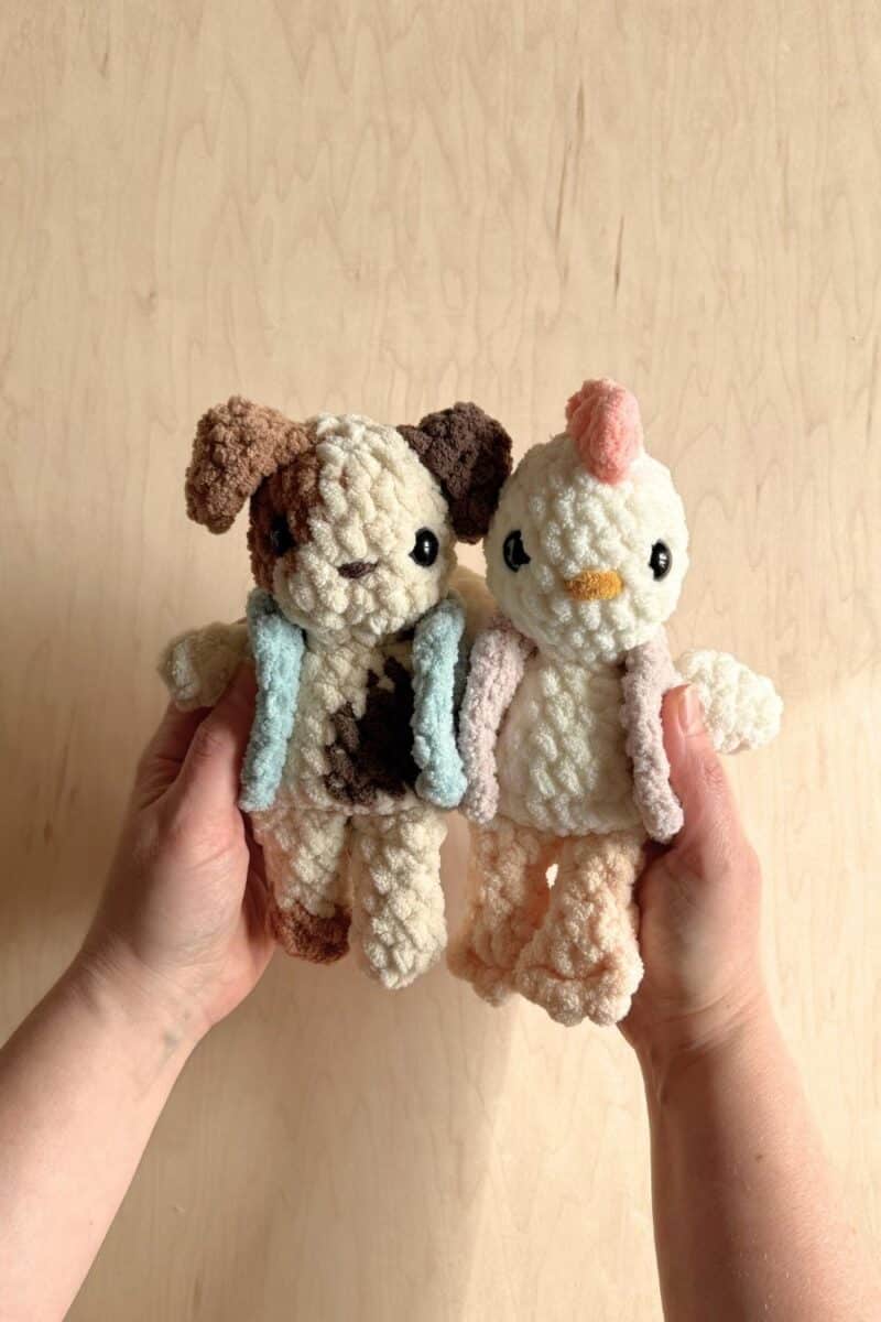 Hands holding two crochet animals wearing crochet vests.