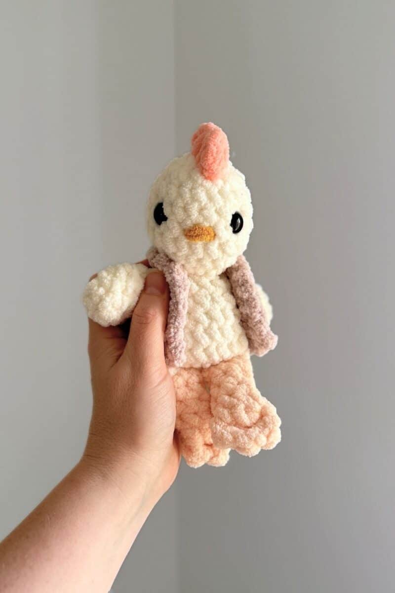 Hand holding a little white crochet chicken wearing a crochet vest.