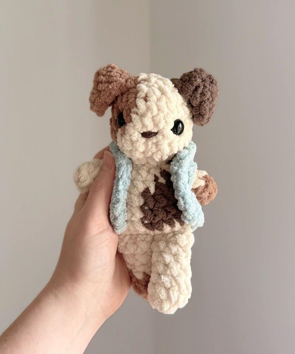 Hand holding a crochet puppy with spots and wearing a crochet vest.