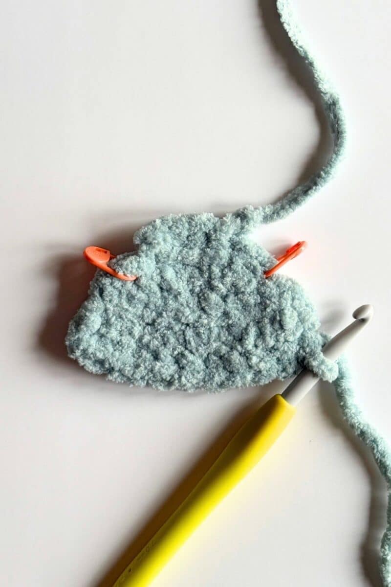 Process photo of a blue crochet vest with stitch markers.