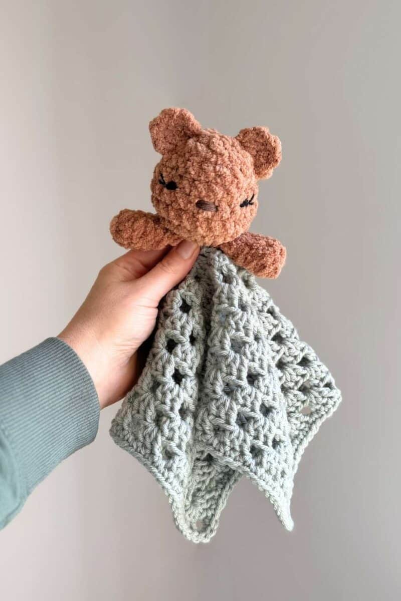 A brown bear crochet lovey with blue blanket.