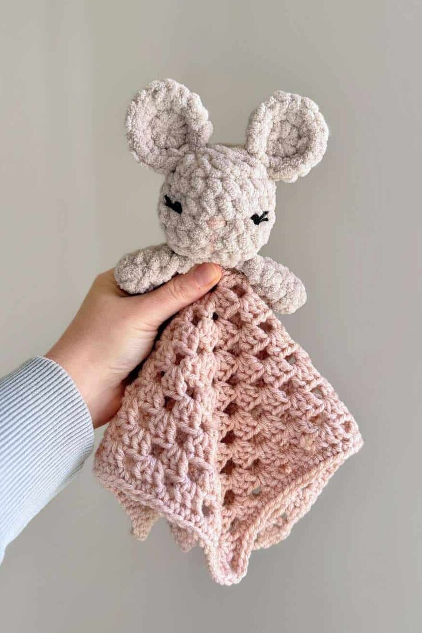 A grey mouse crochet lovey with a pink blanket.