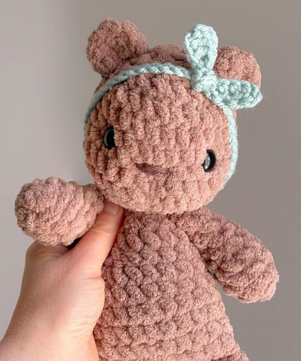 A brown crochet bear wearing a blue crochet headband.