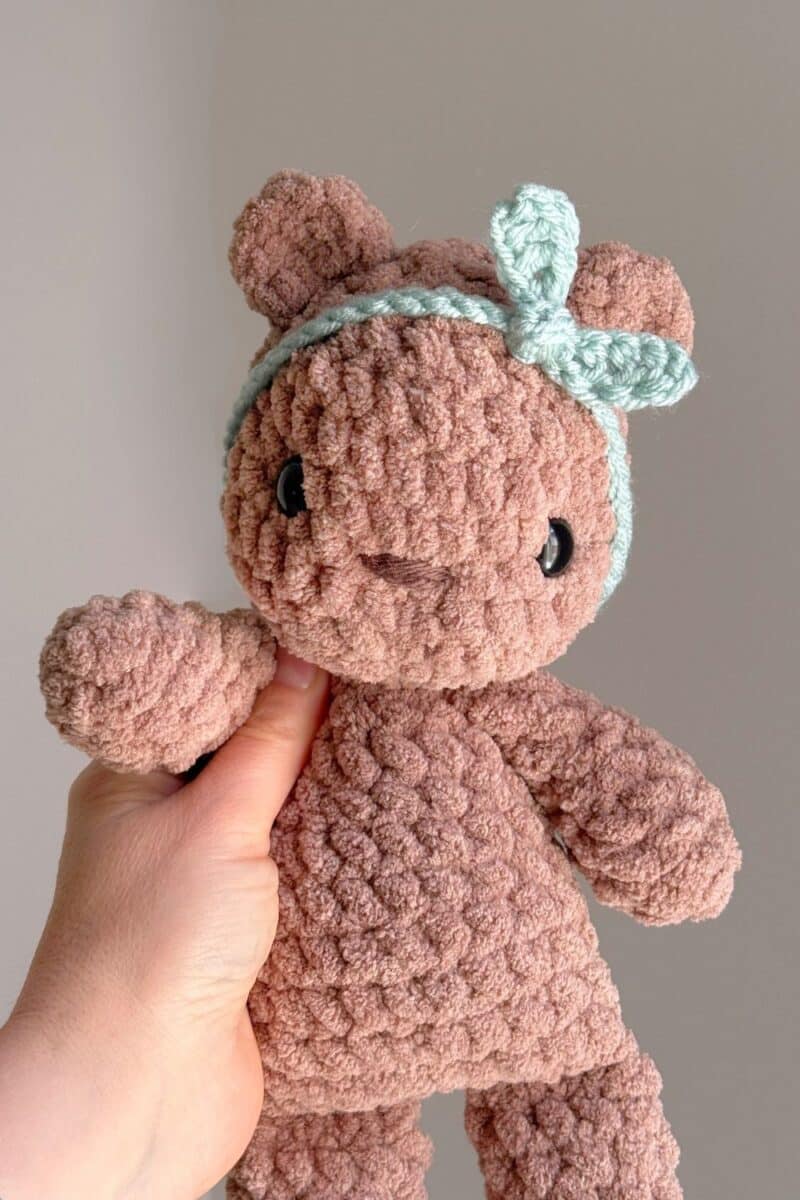 A brown crochet teddy bear wearing a blue headband.
