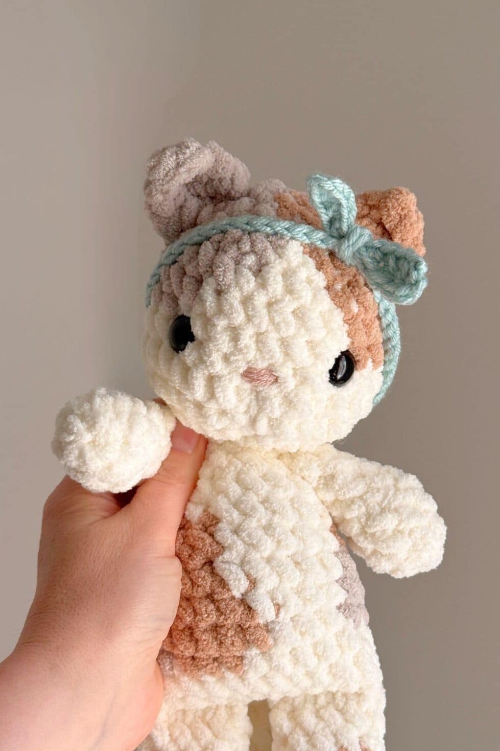 A crochet kitty with light calico coloring wearing a little crochet headband.