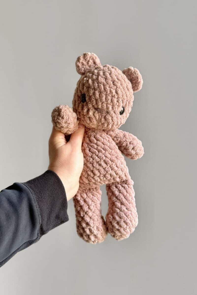 A hand holding a light brown crochet bear.