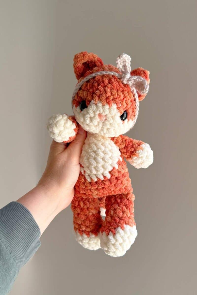 An orange and white crochet tabby cat wearing a crochet headband.