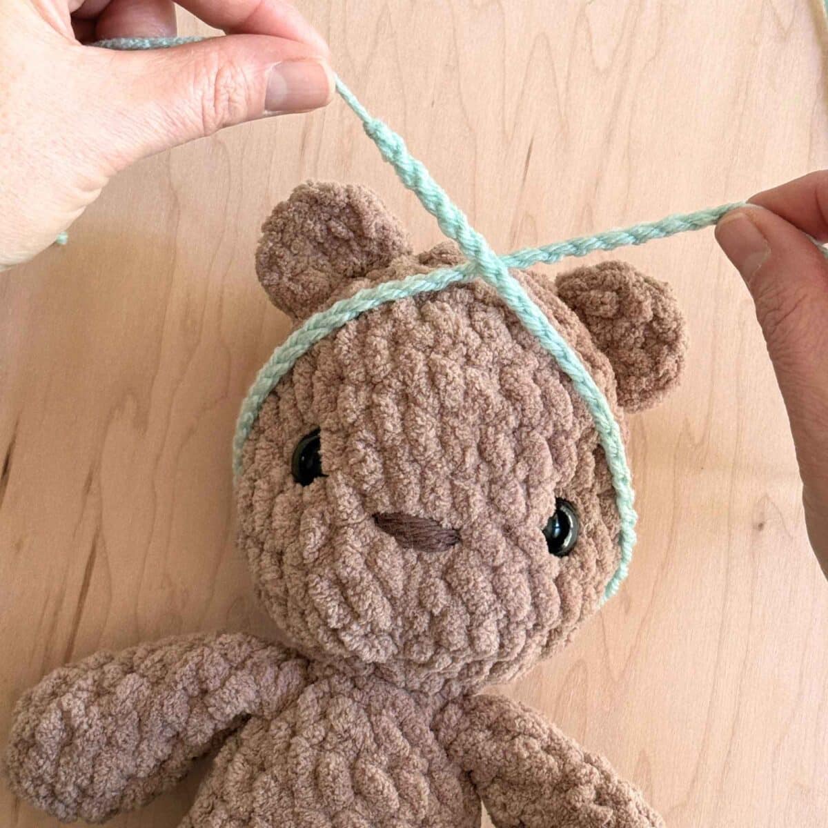 A crochet bear with a partially finished headband wrapped around the head for sizing.