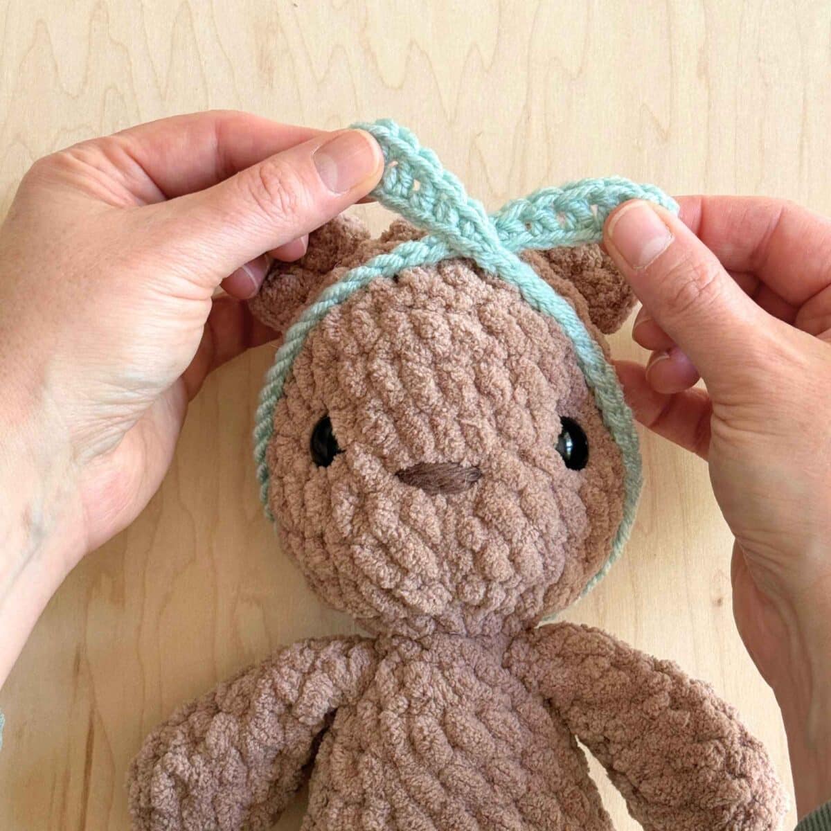 Hands showing how to line up the headband for knotting onto the head of the crochet bear.