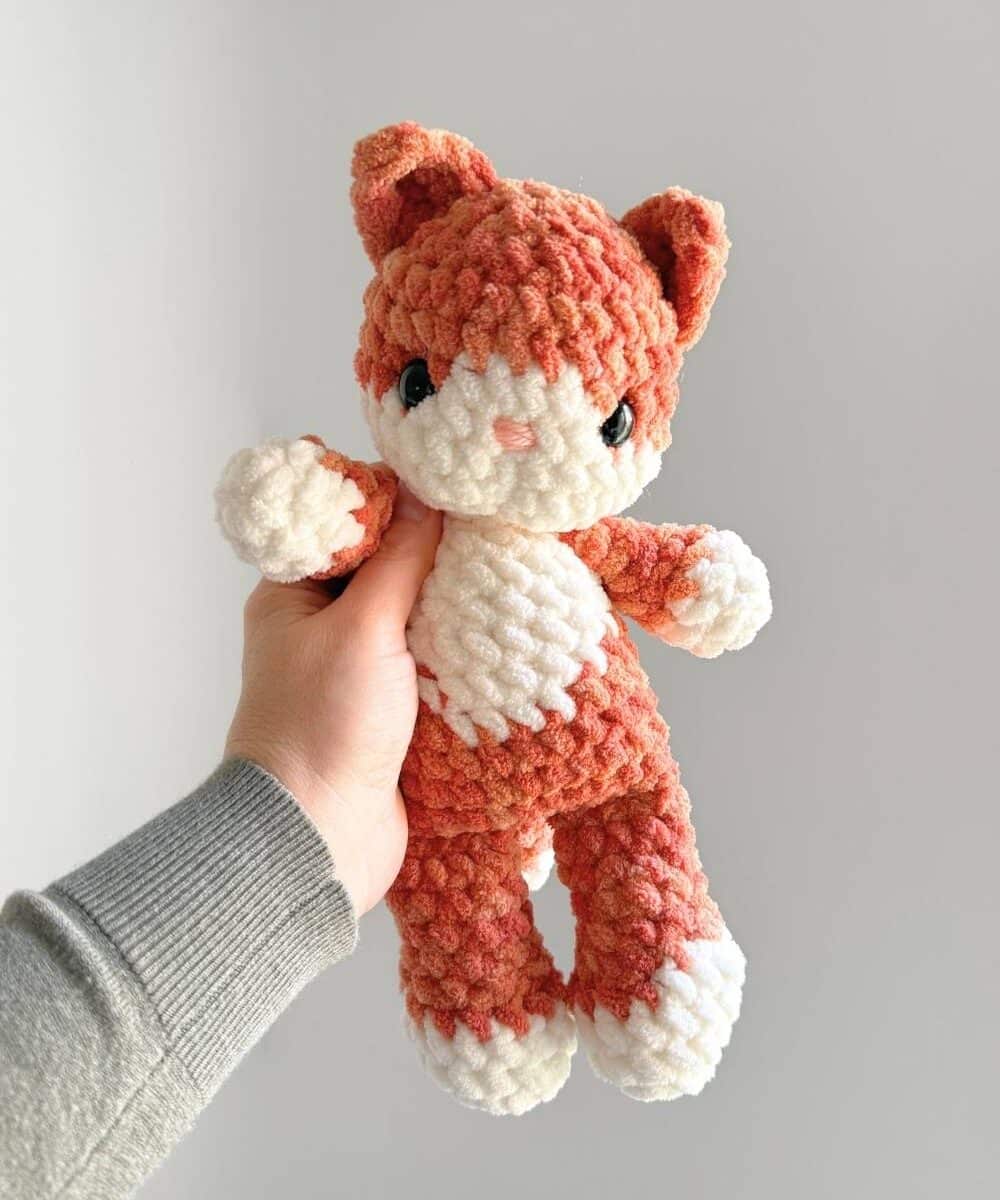 Hand holding an orange and cream crochet kitty.