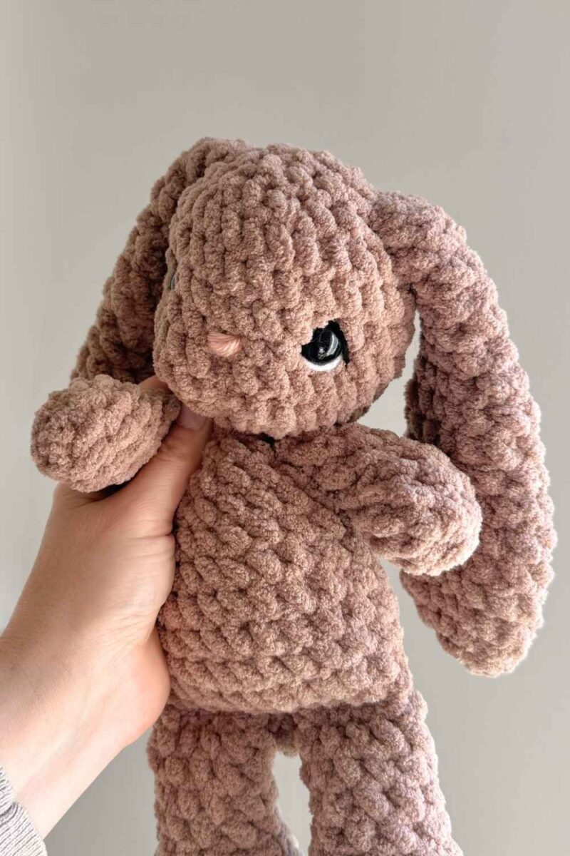 A brown crochet bunny with floppy ears. She has details embroidered on her eyes.