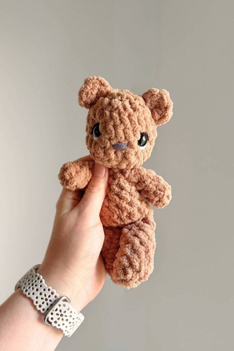 A tiny brown crochet teddy bear with embroidery added to it's safety eyes.