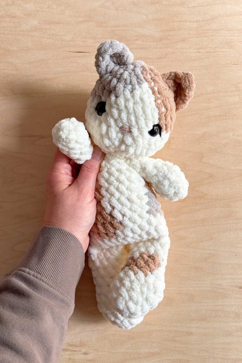 Hand holding a crochet cat with grey and cream details.