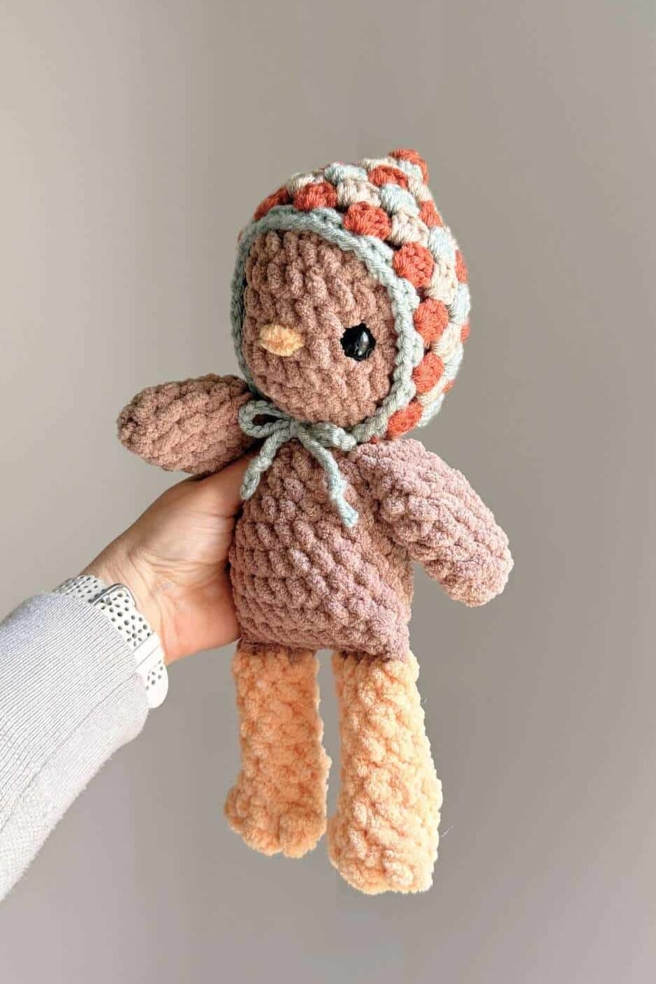 A light brown crochet chicken wearing a little crochet multicolored hat.