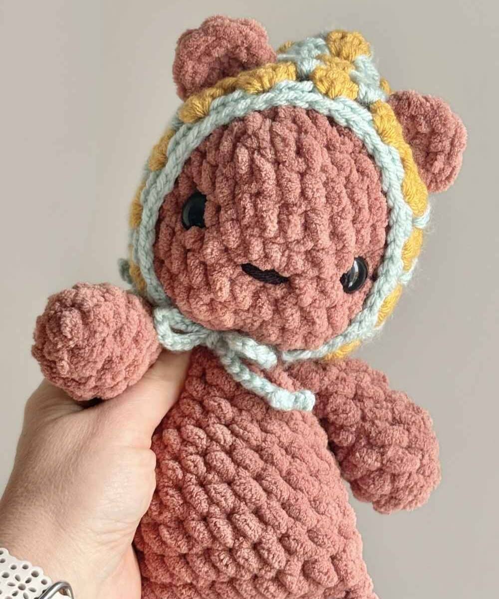 A brown crochet teddy bear wearing a vintage granny square style hat.