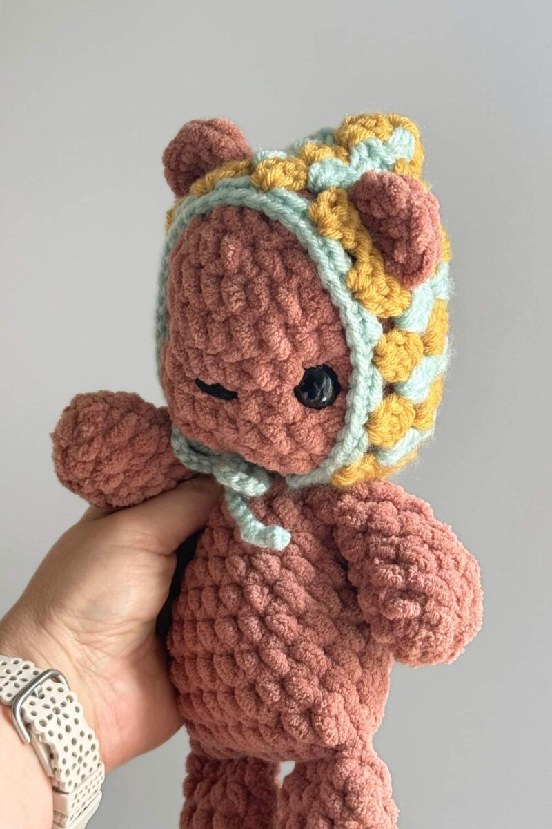 Hand holding a brown crochet bear wearing a crochet granny square inspired hat.