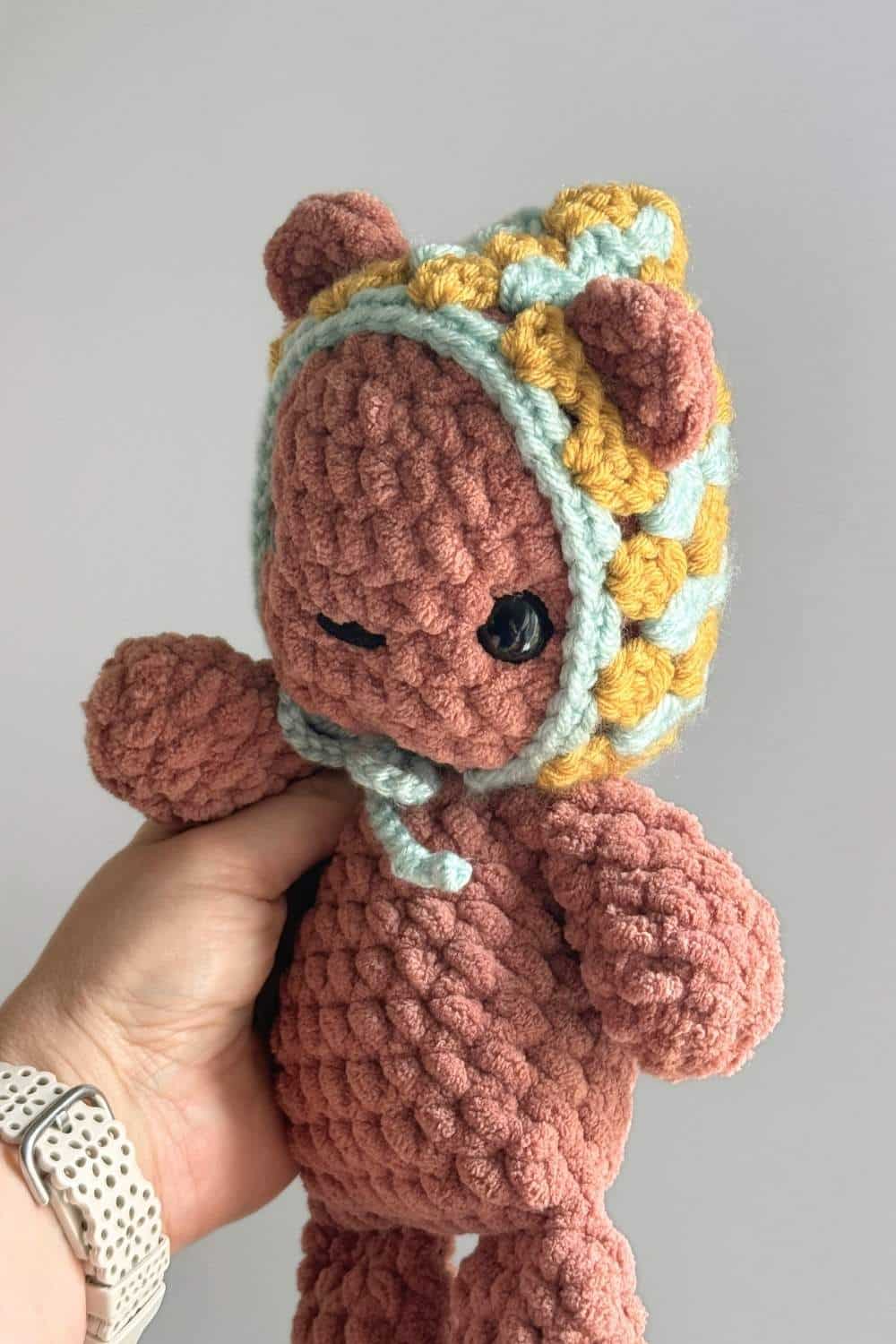 A brown crochet teddy bear wearing a granny square crochet hat.
