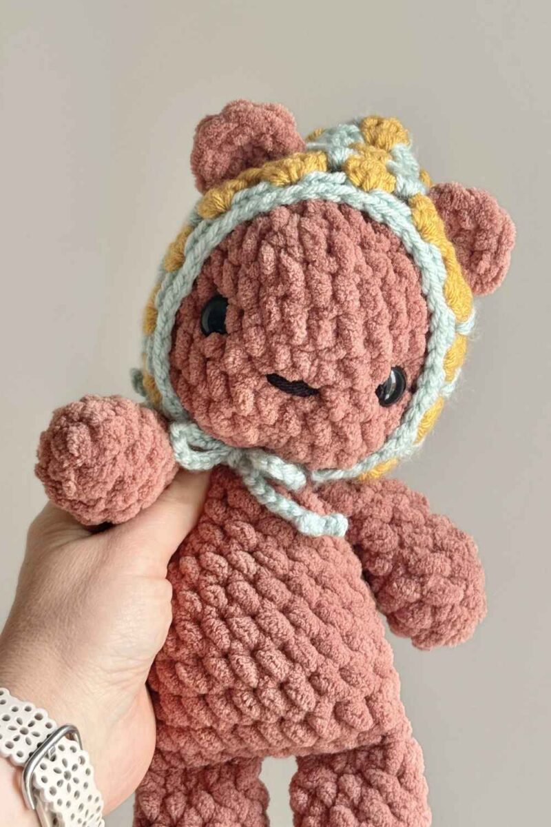 A chocolate brown crochet bear wearing a yellow and blue crochet Pixie Hat.