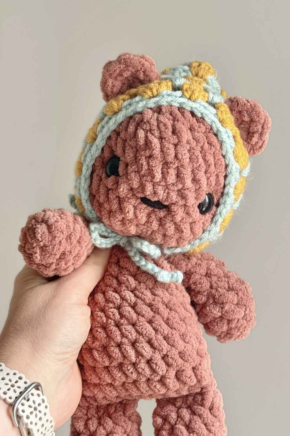 A brown crochet teddy bear wearing a vintage granny square style hat.